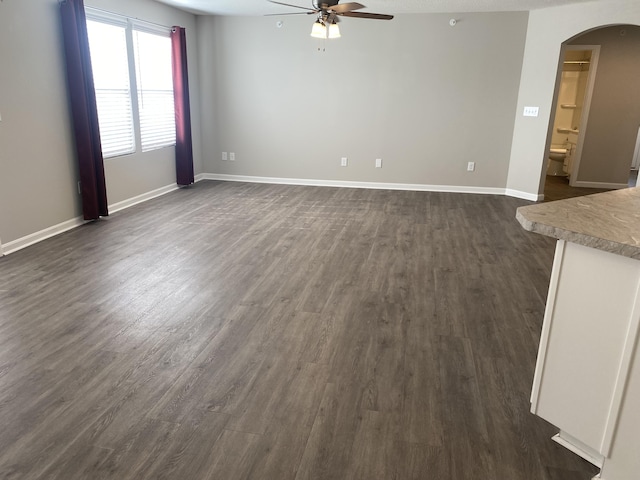 unfurnished living room featuring dark wood finished floors, ceiling fan, arched walkways, and baseboards