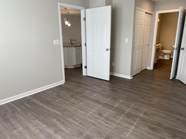 unfurnished bedroom with dark wood-style floors, a sink, a closet, ensuite bath, and baseboards