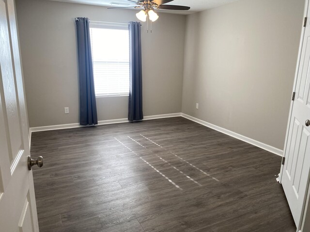empty room with dark wood finished floors, ceiling fan, and baseboards