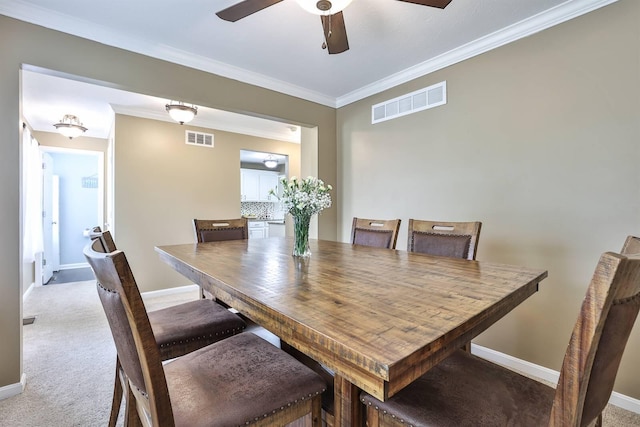 carpeted dining space featuring baseboards, ceiling fan, ornamental molding, and visible vents