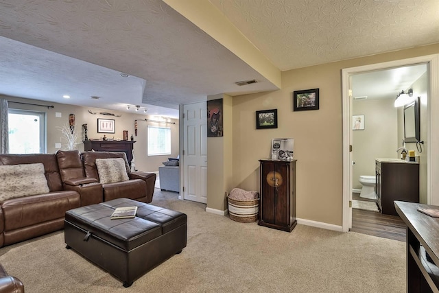 carpeted living room featuring visible vents, a textured ceiling, and baseboards