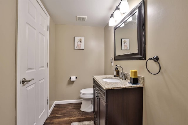 half bath featuring vanity, toilet, baseboards, wood finished floors, and visible vents