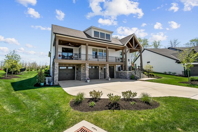 view of front of house with a front lawn, driveway, stone siding, a ceiling fan, and a garage