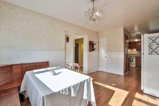dining space with wainscoting, ceiling fan with notable chandelier, and wood finished floors