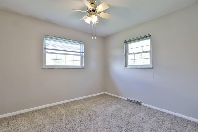 carpeted spare room featuring ceiling fan, baseboards, visible vents, and a wealth of natural light