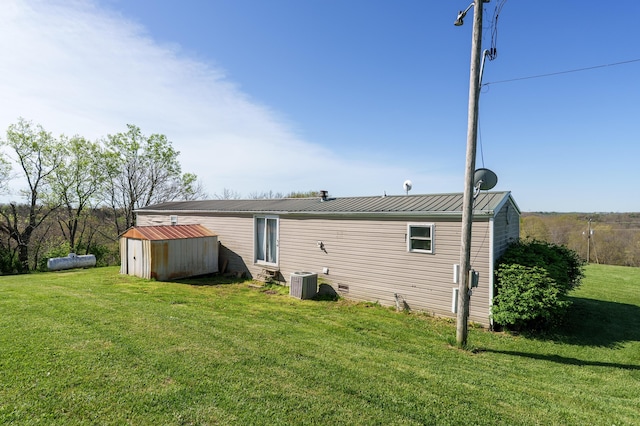 back of property featuring metal roof, an outbuilding, a yard, central AC, and a storage unit