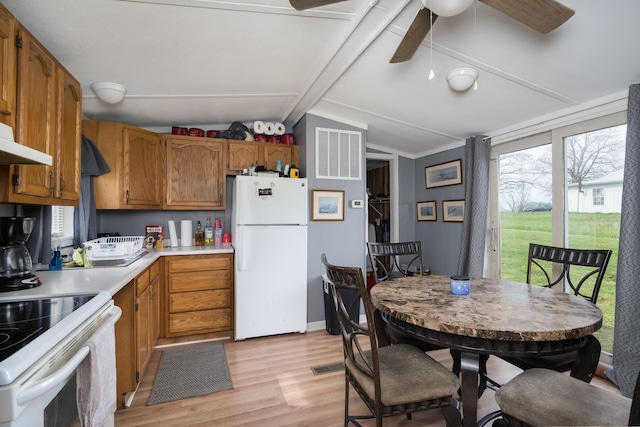 kitchen with lofted ceiling, light countertops, light wood finished floors, white appliances, and brown cabinetry