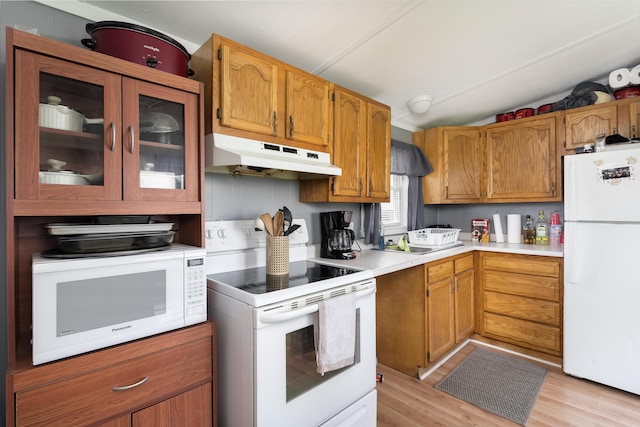 kitchen with light wood-style flooring, light countertops, under cabinet range hood, vaulted ceiling, and white appliances