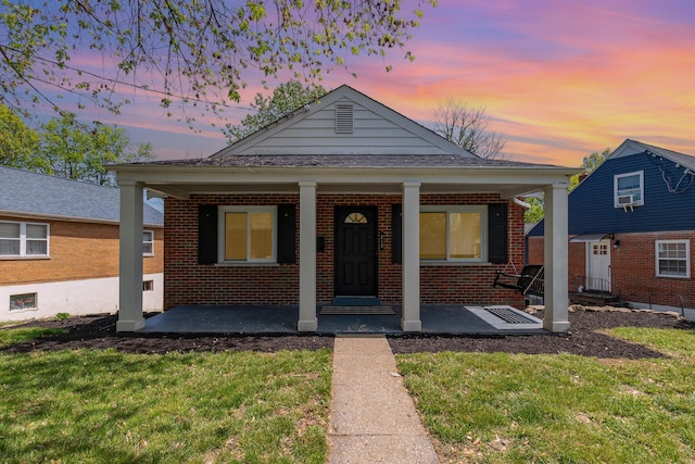 bungalow-style house featuring covered porch, brick siding, and a lawn
