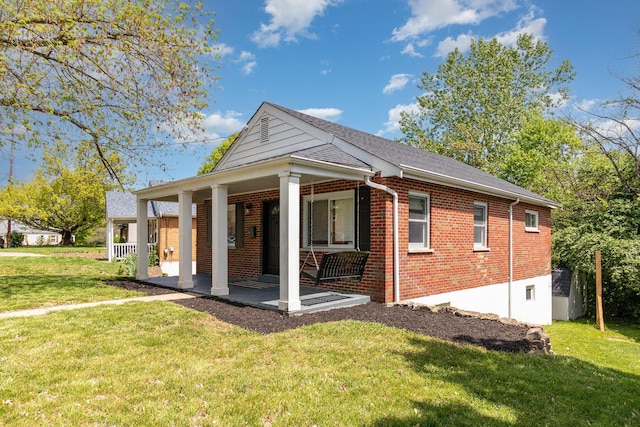back of house with roof with shingles, covered porch, a yard, and brick siding