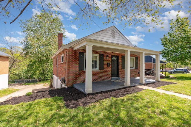 bungalow-style house featuring brick siding, a front yard, a chimney, and covered porch