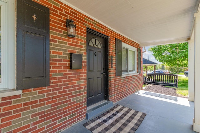 doorway to property featuring a porch and brick siding