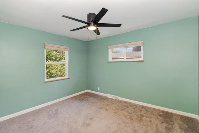 carpeted empty room featuring baseboards, a wealth of natural light, a ceiling fan, and visible vents