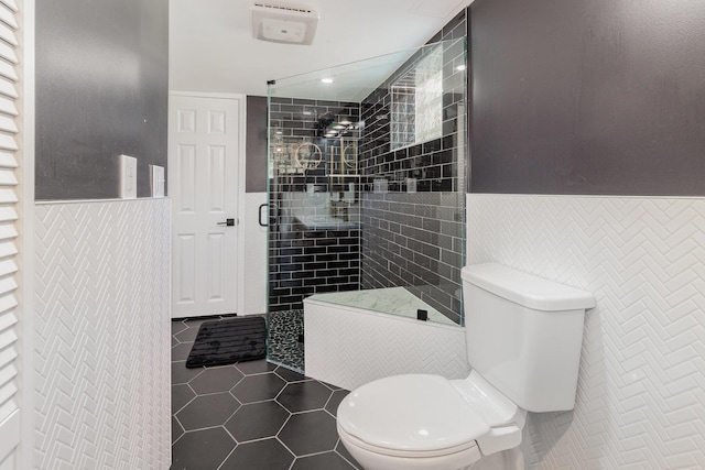 full bath featuring tile walls, tile patterned flooring, a stall shower, a wainscoted wall, and toilet