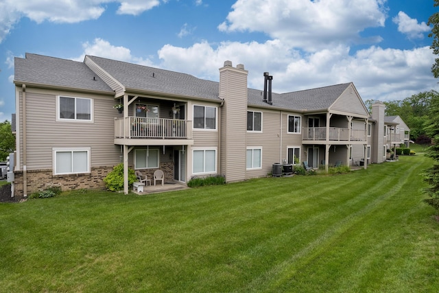 back of property featuring a balcony, a chimney, a yard, and a patio
