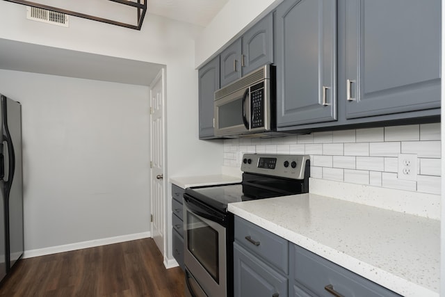 kitchen with stainless steel appliances, gray cabinetry, dark wood finished floors, and tasteful backsplash