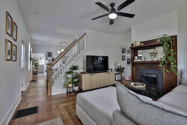 living area featuring stairs, ceiling fan, a fireplace, baseboards, and visible vents