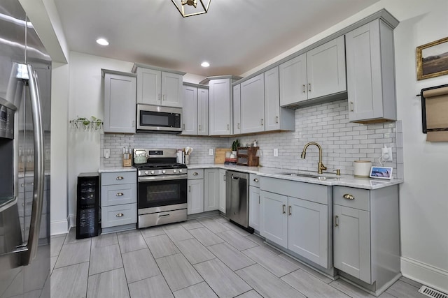 kitchen featuring stainless steel appliances, gray cabinetry, baseboards, and a sink
