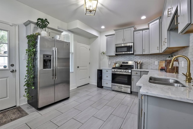 kitchen with appliances with stainless steel finishes, light stone countertops, gray cabinets, and a sink
