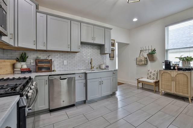 kitchen with gray cabinets, stainless steel appliances, decorative backsplash, and a sink