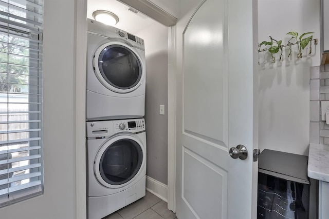 clothes washing area featuring light tile patterned floors, stacked washer and clothes dryer, a healthy amount of sunlight, and laundry area