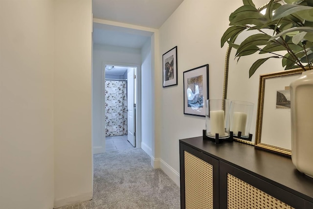 hallway featuring light colored carpet and baseboards