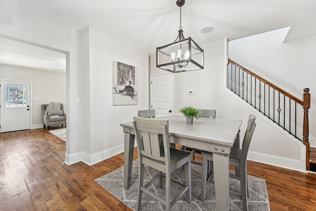 dining area featuring an inviting chandelier, baseboards, wood finished floors, and stairway