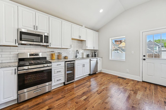 kitchen with appliances with stainless steel finishes, a sink, tasteful backsplash, wine cooler, and vaulted ceiling
