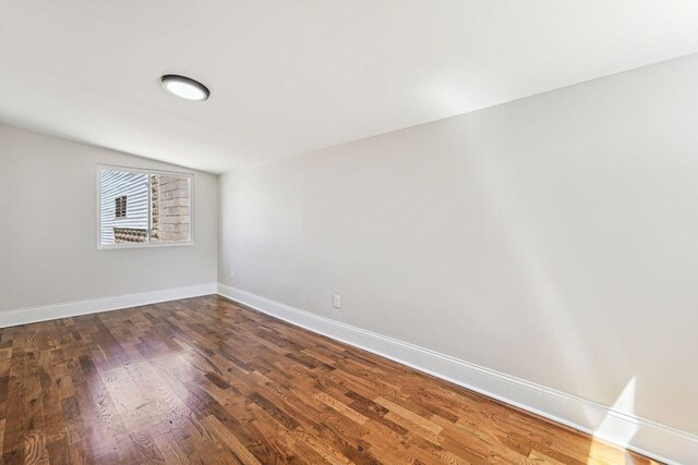 unfurnished room featuring baseboards, dark wood finished floors, and lofted ceiling