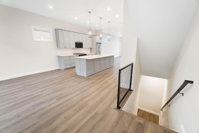 kitchen featuring gray cabinets, light countertops, light wood finished floors, baseboards, and a center island with sink