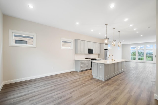 kitchen with baseboards, an island with sink, light wood-style floors, and appliances with stainless steel finishes