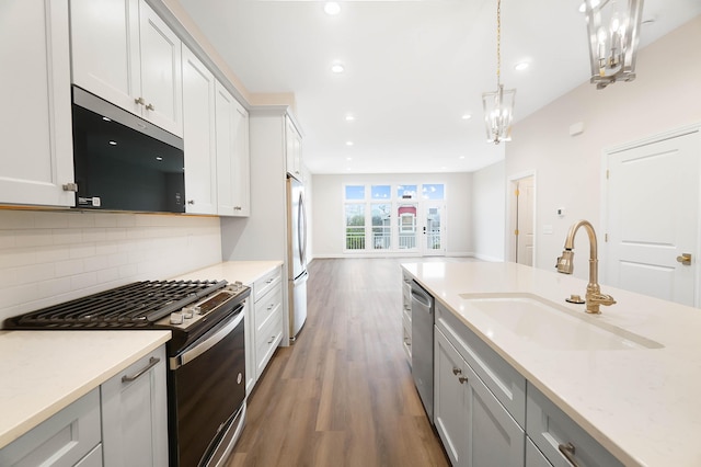 kitchen featuring a sink, tasteful backsplash, dark wood-type flooring, pendant lighting, and appliances with stainless steel finishes