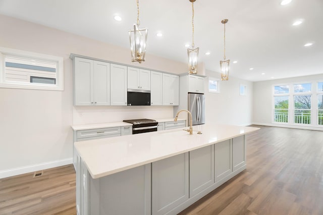 kitchen featuring recessed lighting, a kitchen island with sink, appliances with stainless steel finishes, a sink, and light wood-type flooring