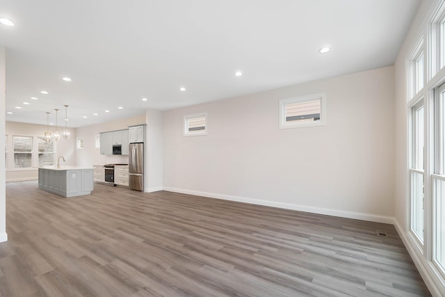unfurnished living room with light wood finished floors, recessed lighting, a sink, and baseboards