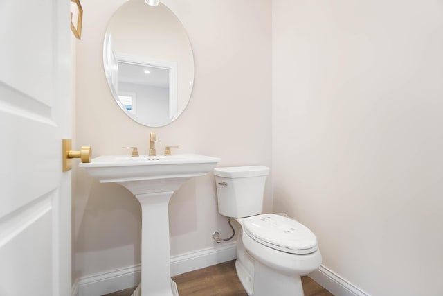 half bathroom featuring wood finished floors, toilet, and baseboards