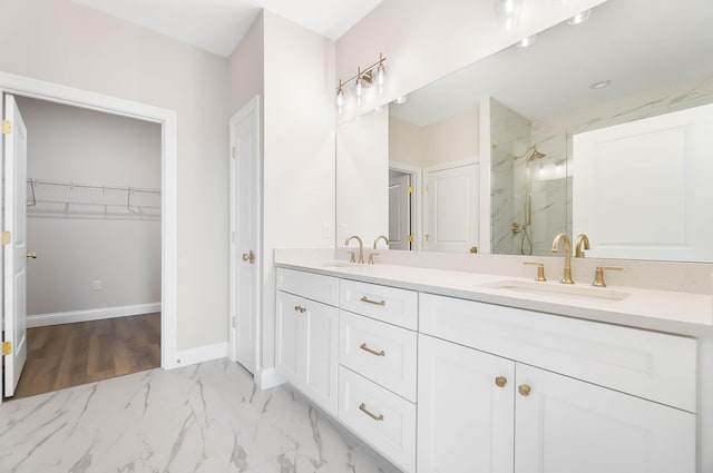 bathroom featuring a spacious closet, a marble finish shower, double vanity, and a sink