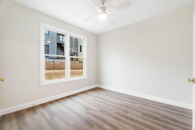 empty room with wood finished floors, ceiling fan, visible vents, and baseboards