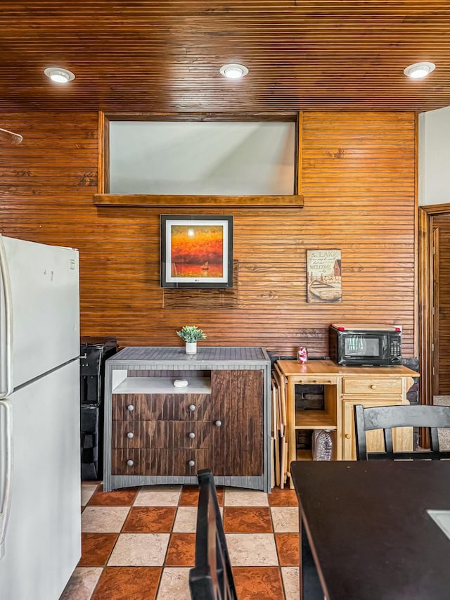 kitchen with wooden walls, wooden ceiling, freestanding refrigerator, and black microwave