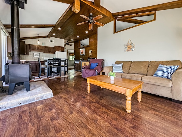 living area featuring lofted ceiling with beams, a wood stove, a ceiling fan, wood finished floors, and visible vents