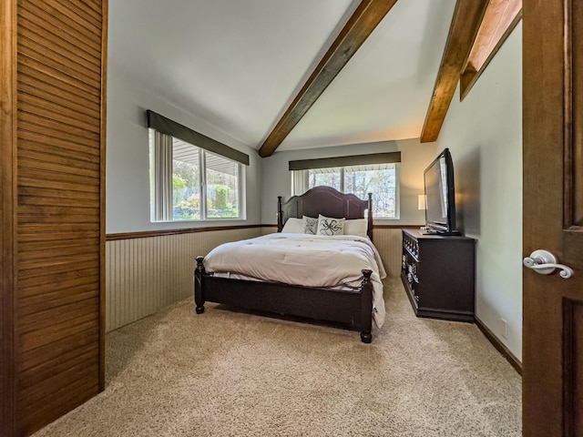 bedroom featuring carpet floors, lofted ceiling with beams, multiple windows, and a wainscoted wall
