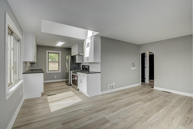 kitchen with visible vents, dark countertops, appliances with stainless steel finishes, arched walkways, and light wood-style floors
