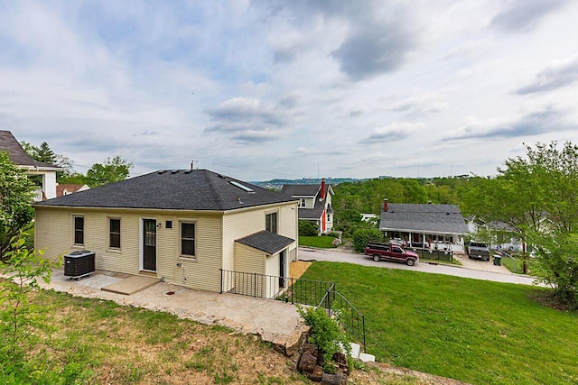 back of house with central air condition unit, fence, a shingled roof, and a yard