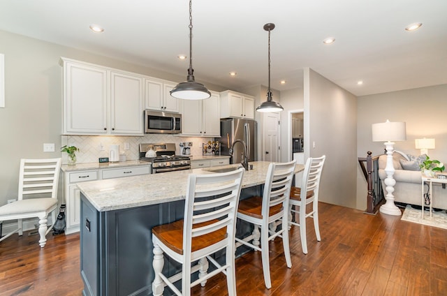 kitchen with stainless steel appliances, backsplash, white cabinetry, dark wood-style floors, and a center island with sink