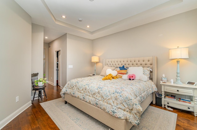 bedroom with recessed lighting, baseboards, wood finished floors, and a tray ceiling