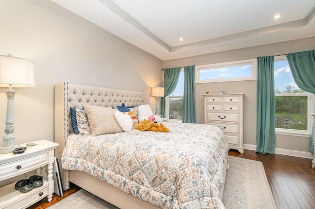 bedroom with dark wood-type flooring, recessed lighting, a tray ceiling, and baseboards