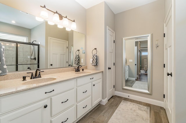 ensuite bathroom featuring a stall shower, double vanity, a sink, and wood finished floors