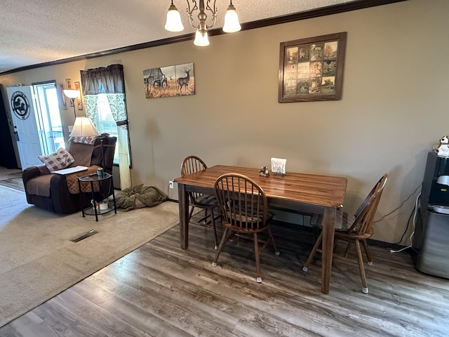 dining space with a textured ceiling, visible vents, ornamental molding, wood finished floors, and a notable chandelier