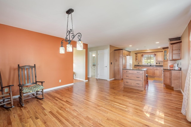 kitchen featuring freestanding refrigerator, glass insert cabinets, baseboards, a sink, and light wood finished floors