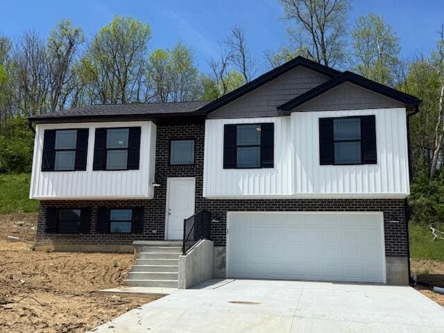 raised ranch featuring a garage, driveway, and brick siding