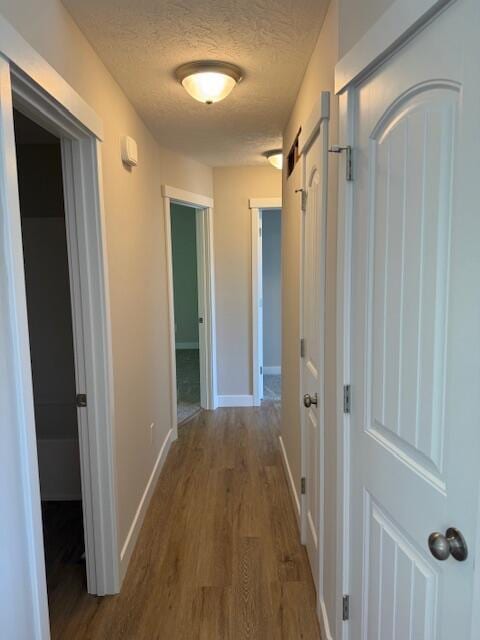 corridor featuring baseboards, a barn door, a textured ceiling, and wood finished floors
